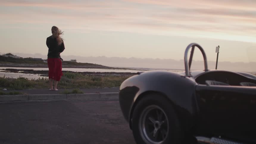 A woman stands in the wind by the car