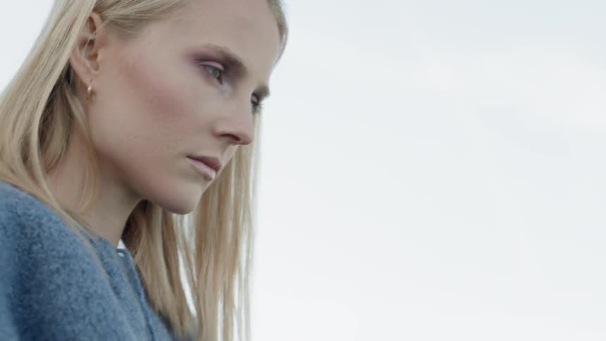 Woman with blond hair turns her head under a cloudy sky