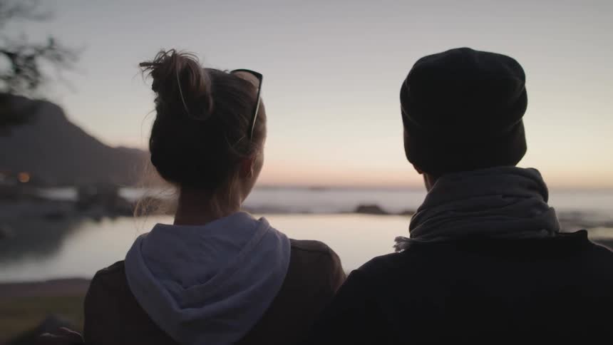 Two people watch the sunset together by the shore