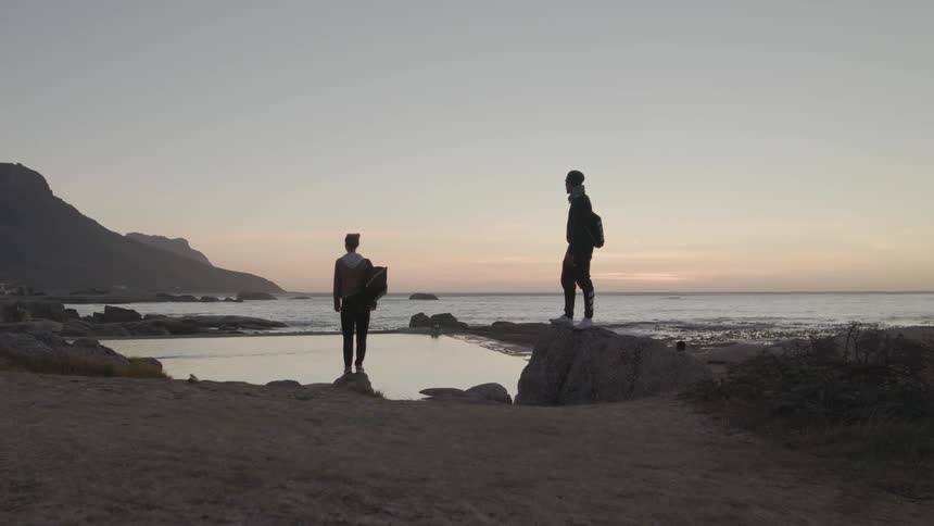 Two people stand by the shore looking at the sunset