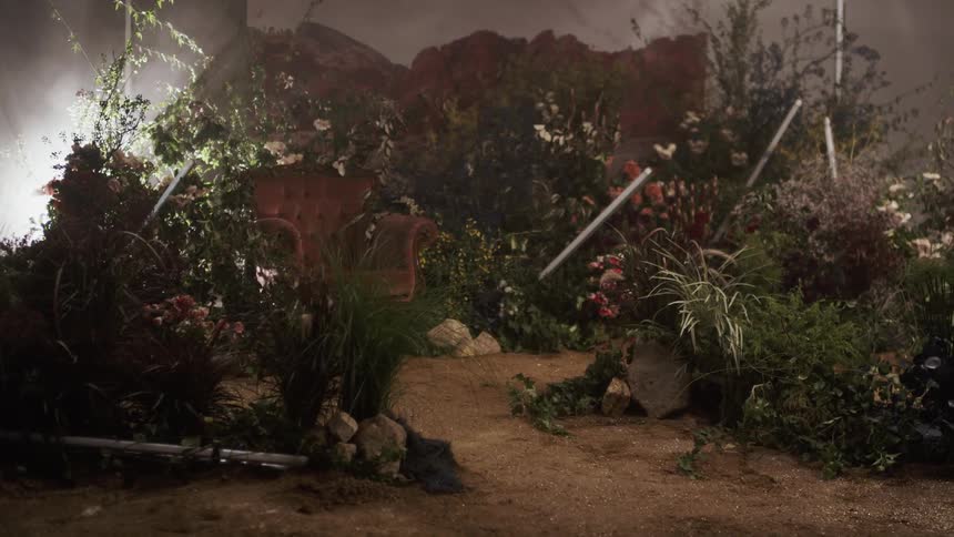 Fluorescent lights are flashing as they stand arranged on a set with flowers and dirt