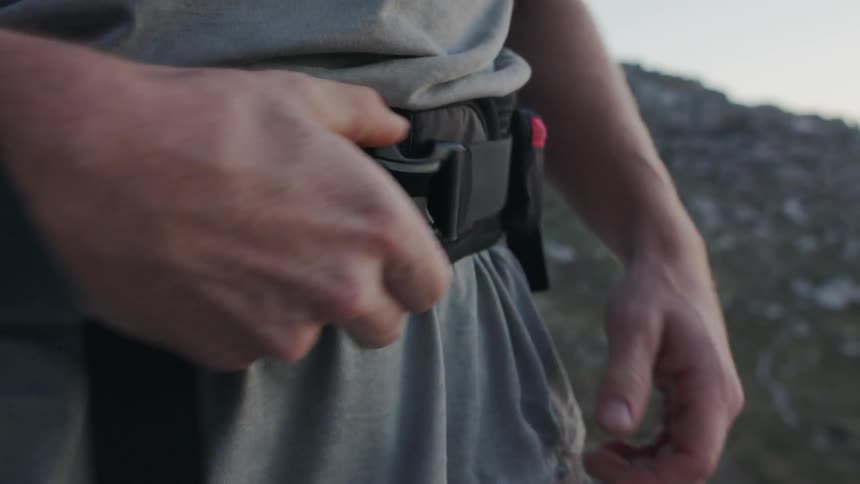 Man unbuckles the belt of his backpack outside on a windy day
