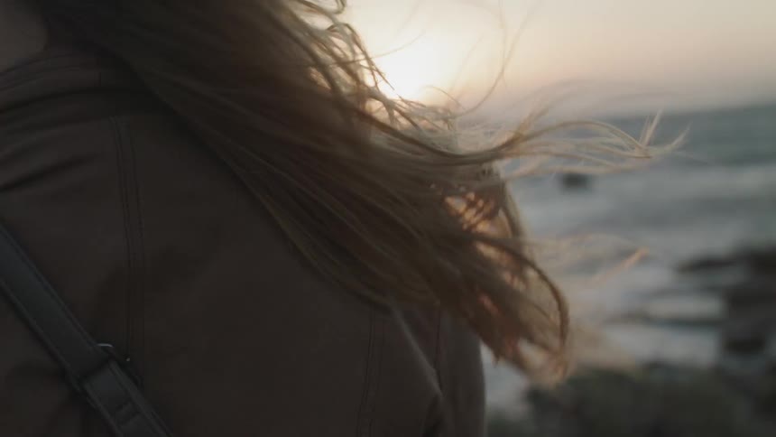 The wind is blowing the woman's hair near the shore