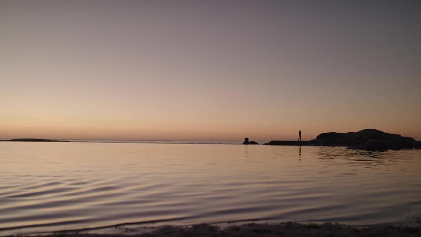 The water in the lake ripples as a person walks on the rocks