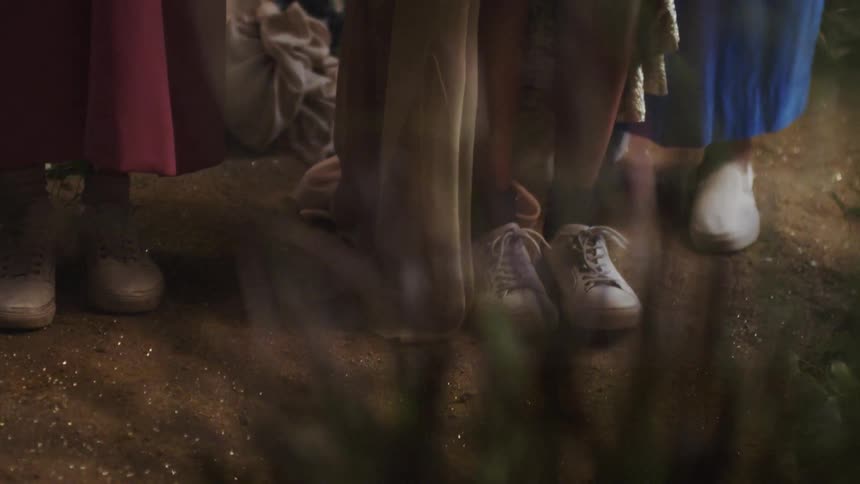 Two people wearing white sneakers stand in dirt
