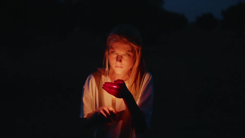 A woman holds a burning candle at night