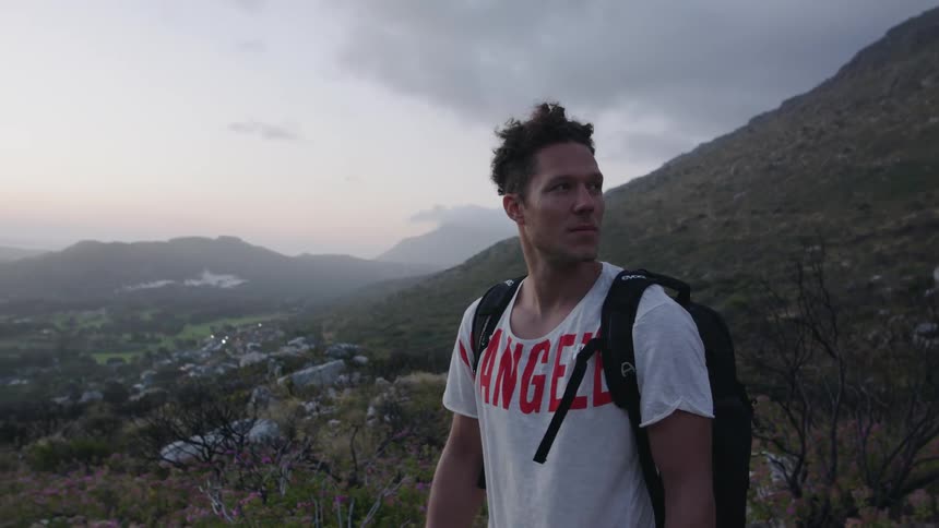 A man is standing in a hilly landscape at dusk on a windy day