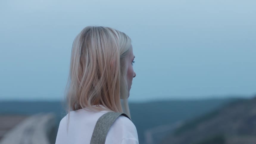 Woman with blond hair blinks her eyes under a blue sky