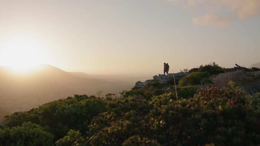 A hiker is walking toward the edge of a mountain at sunset