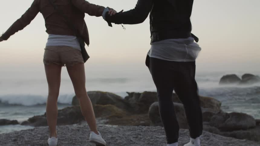 A man and woman hold hands as they balance on a rock on a windy day