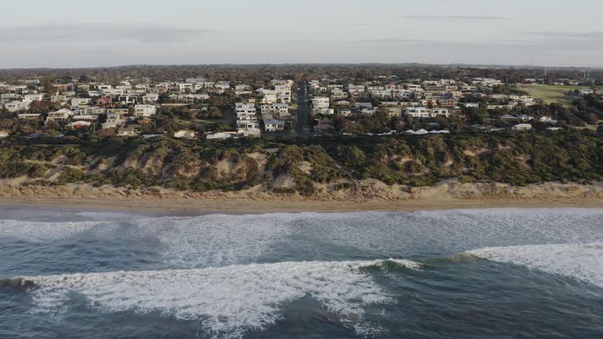 Ocean waves splashing to a sandy shore with a village nearby