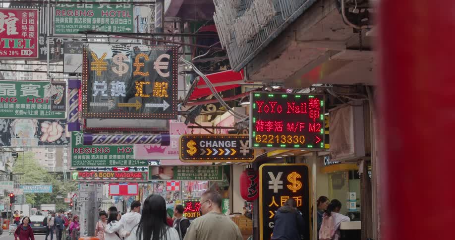People walk on a city sidewalk under flashing store signs