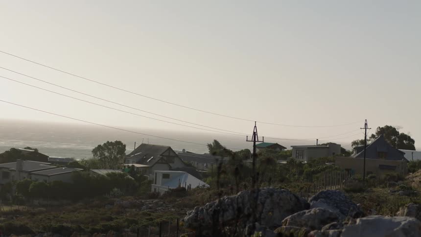 The wind is blowing power lines and tree tops along a coastal community during the day
