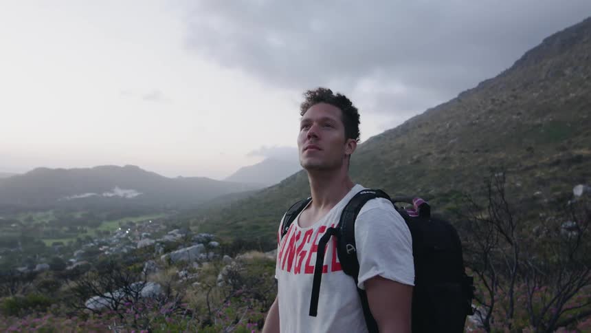 A man wearing a backpack is looking around in a natural setting on a windy day