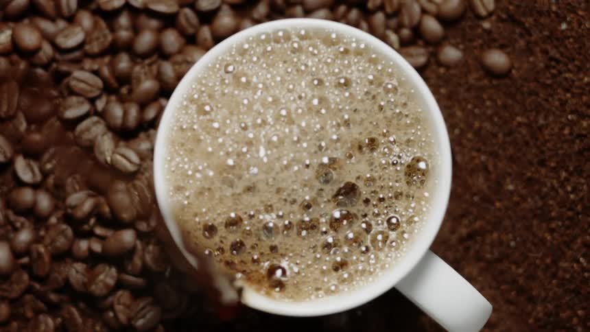 Coffee pours into a mug with beans all around it
