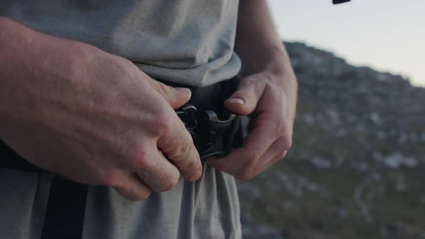 A man is latching the strap on his backpack as he stand outside on a windy day