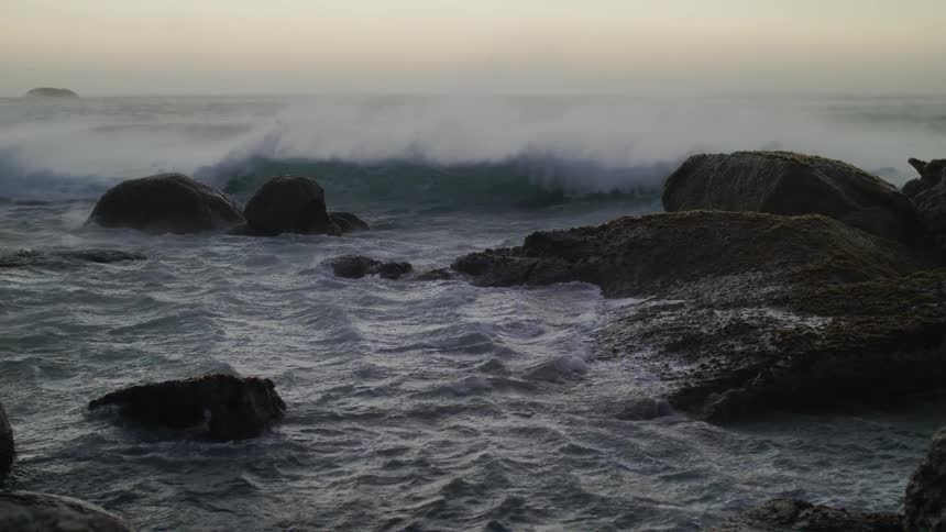 Waves are crashing against rocks at the beach on a windy day
