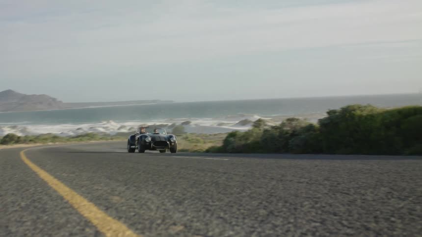 Car speeds down a country road near a large body of water