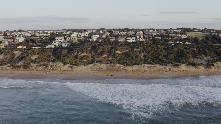 Water splashes to a sandy shore with a village in the distance