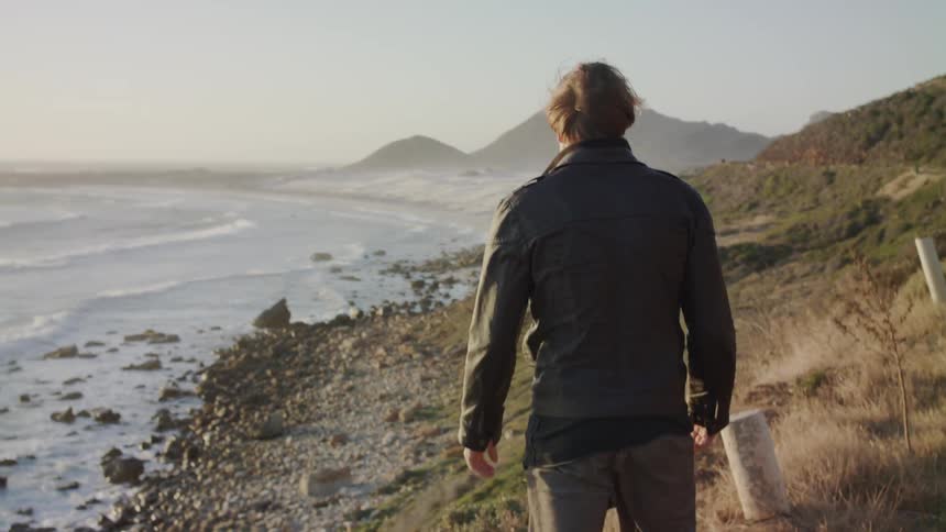The man walks on the hill by the water on a windy day