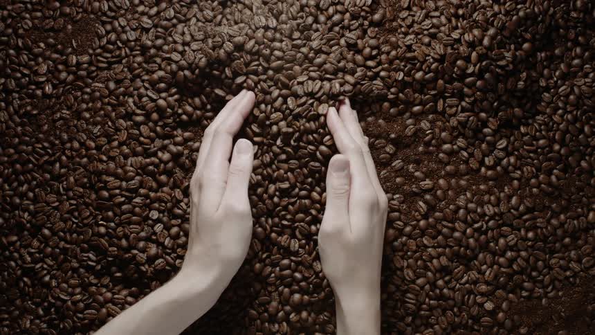 Two hands scoop up coffee beans out of a large pile