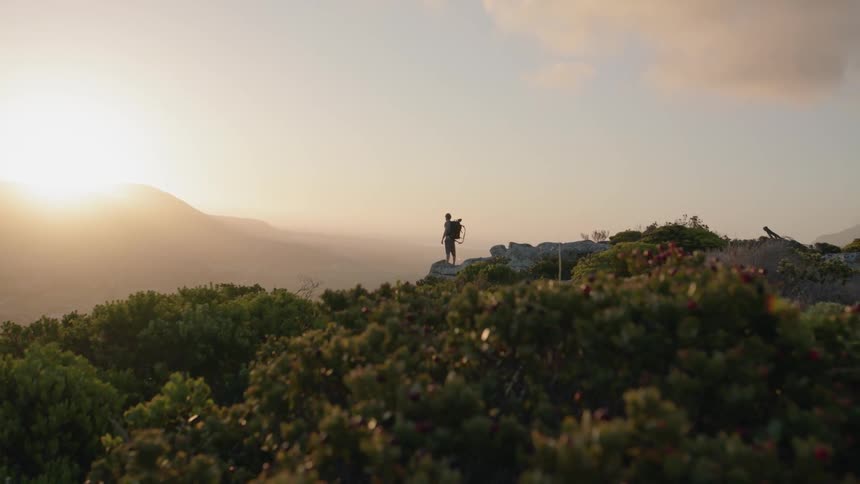 A man wearing a backpack is taking in a mountain view at sunrise