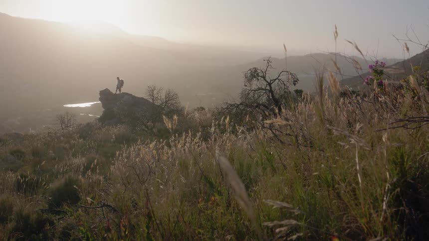 Person stands on a large rock overlooking hills on a sunny day