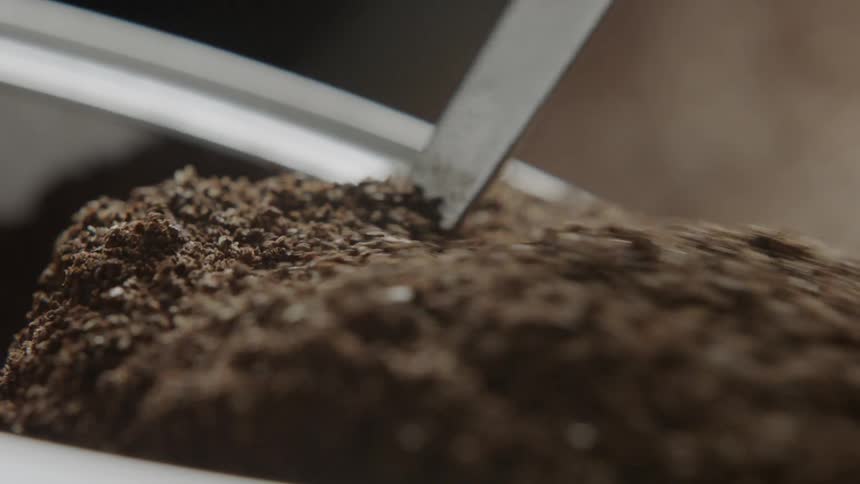 Coffee grounds spill out of a canister and a scoop lifts some grounds up
