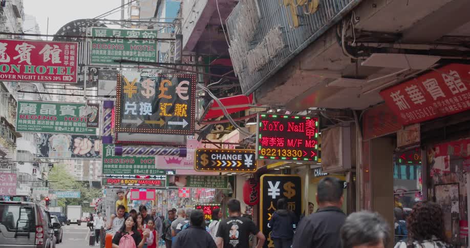 People walk on a city sidewalk under flashing signs