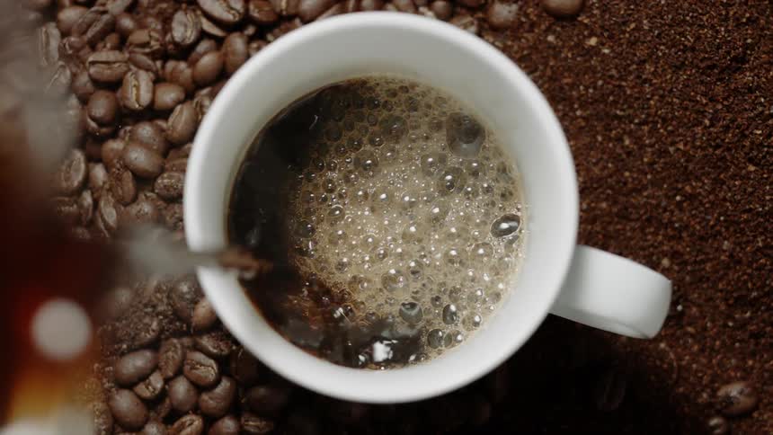 Coffee pours into a mug with beans all around it