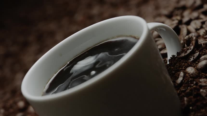 Coffee is dripping into a cup as it sits in a pile of coffee beans