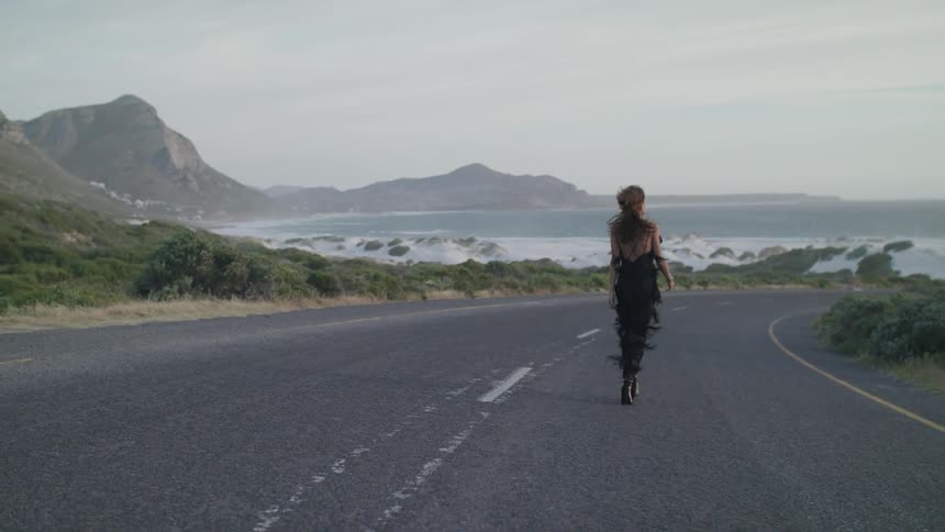 Woman walks down a country road near a large body of water
