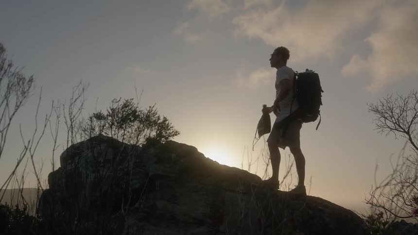Man lifts a backpack as he stands on a rock