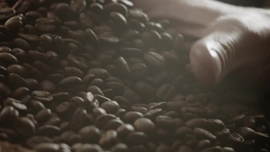 A hand grabs a handful of coffee beans