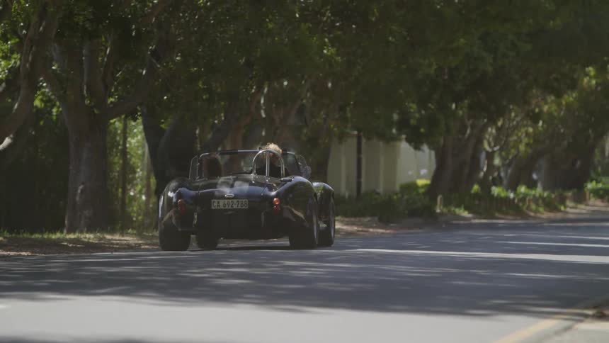 Convertible travels down the street near the trees