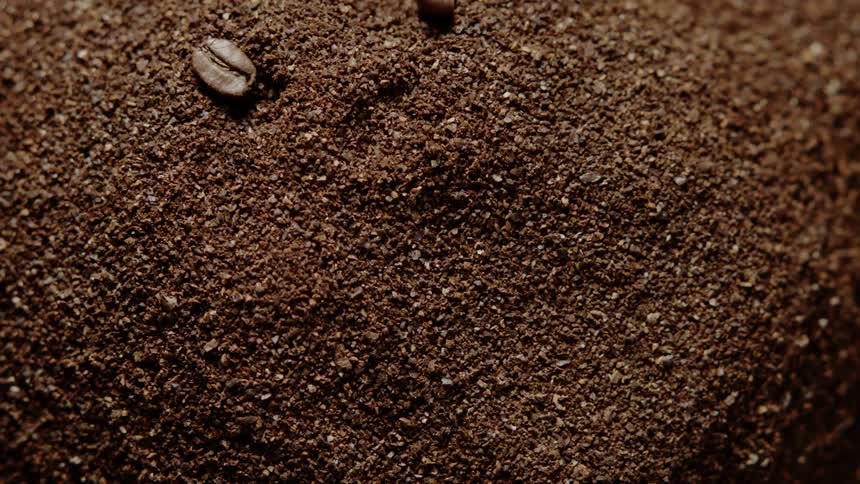 Coffee bean halves fall on a pile of coffee grounds