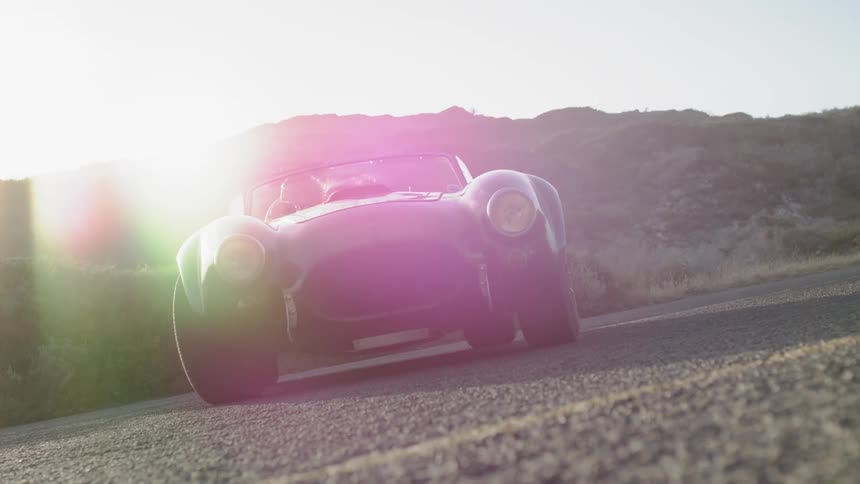 A convertible is parked on a rural road at sunset