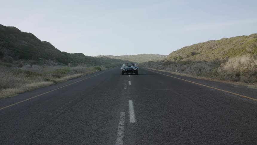 A convertible roadster is making a u-turn in a road and driving off in daylight