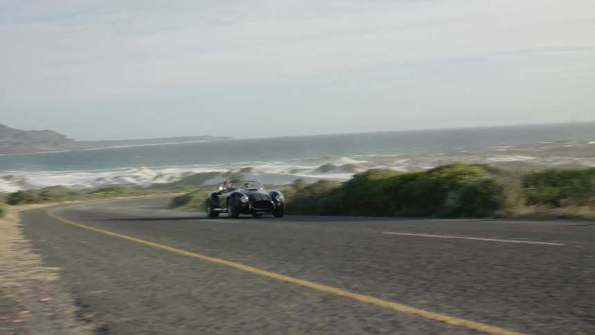 Car speeds down a winding country road on a sunny day