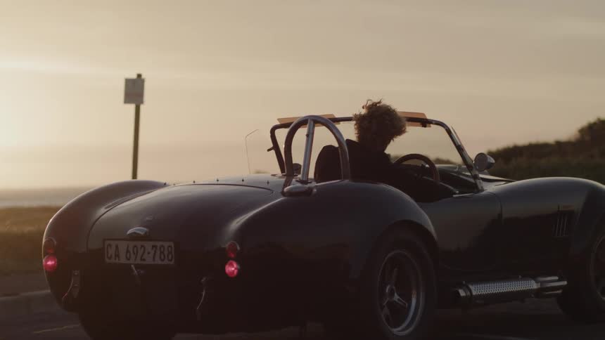 Man is traveling in convertible car at sunset