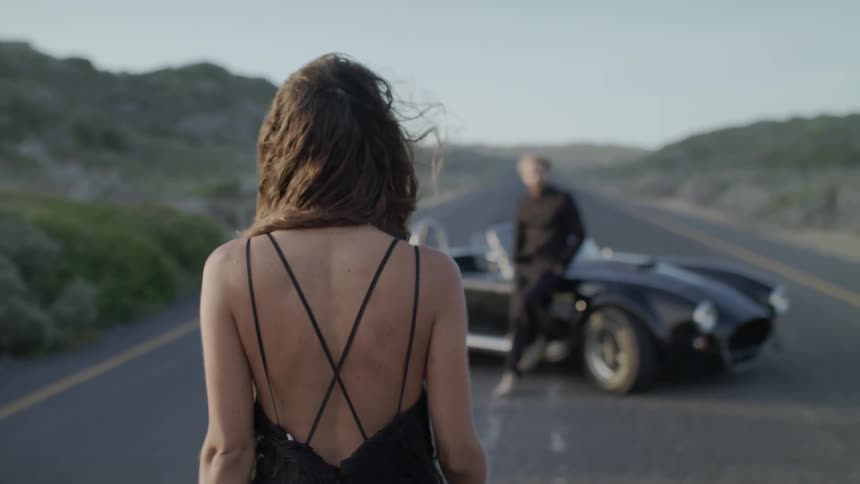 A woman walks on the street towards a convertible car