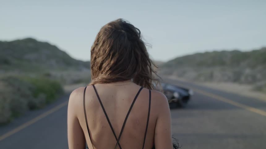 Woman walks towards a convertible parked on a rural road