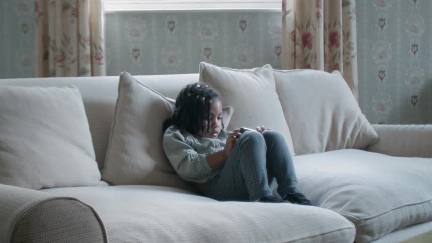 A girl sits on a couch playing with a phone