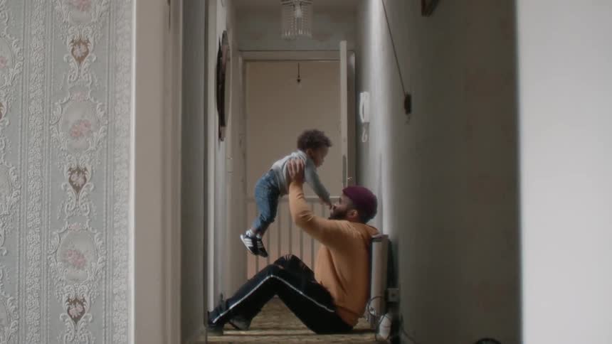 Man sits in a hallway and lifts a small child above his head