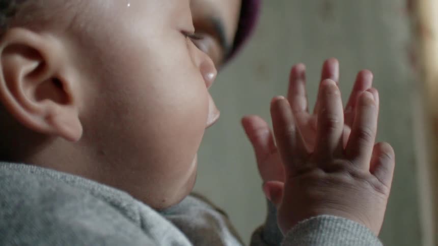 Woman holds a young toddler as he inspects his hands