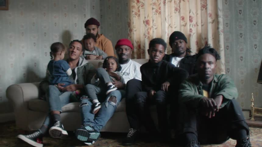 A family of men and boys are gathered on a couch in a living room in daylight