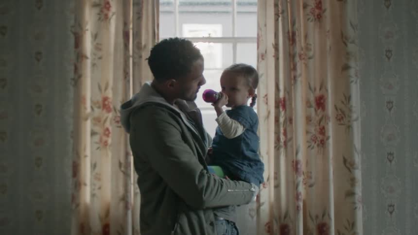 A child drinks from a bottle while being held by dad