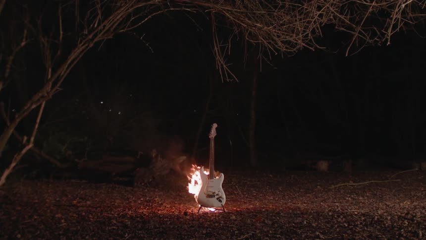 Guitar lit on fire outside in the woods at night
