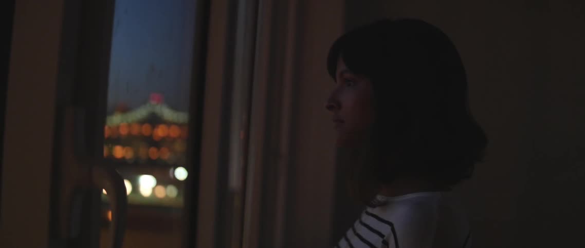 A woman gazes through window at the city at night