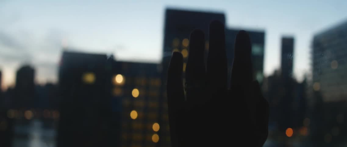 Hand trailing down a window that looks on a lighted city at night